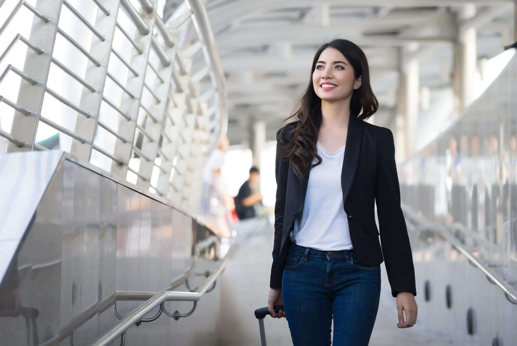 smiling female traveler walking in airport down ramp with luggage