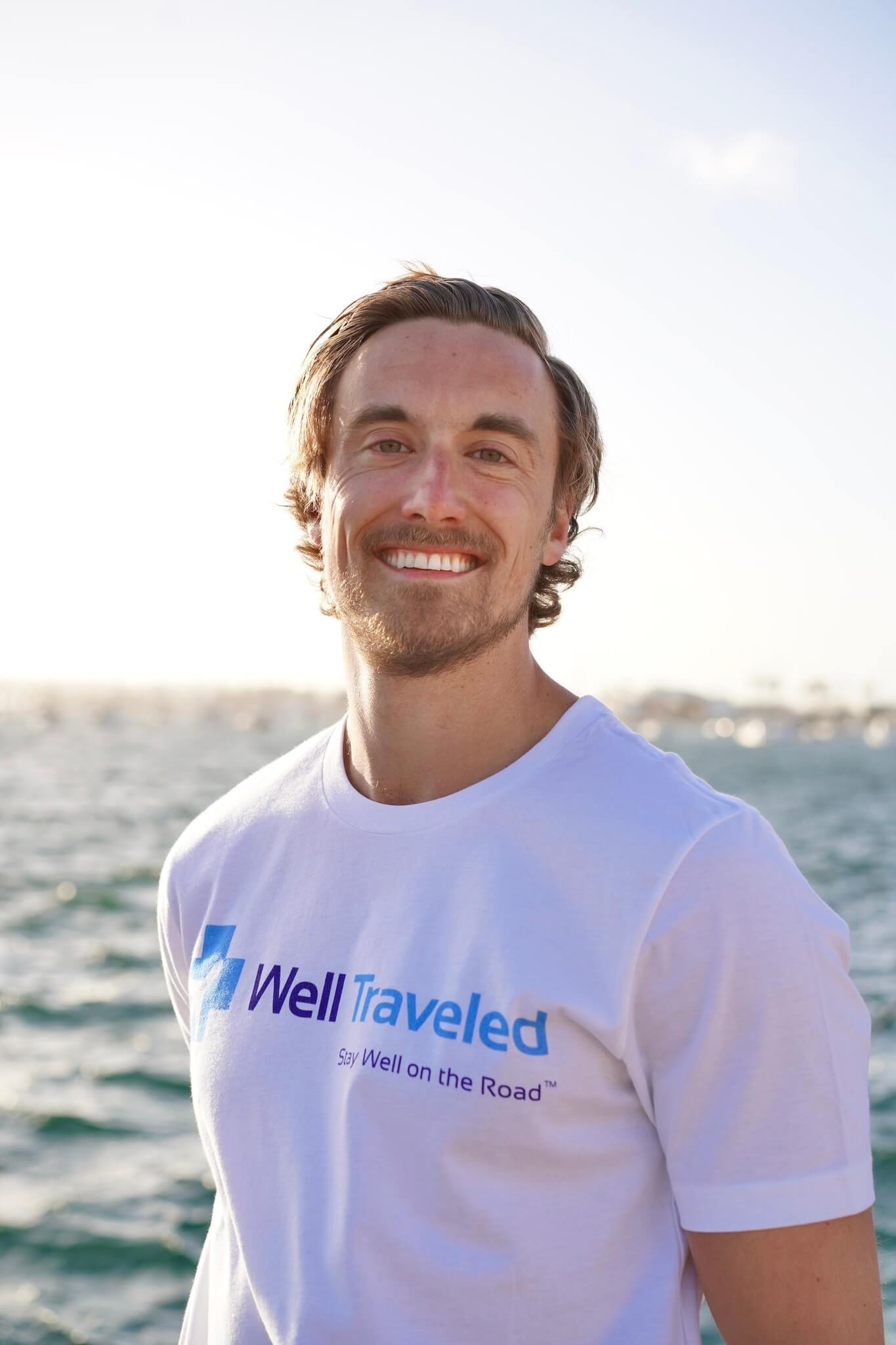 young man in white well traveled shirt smiling by water