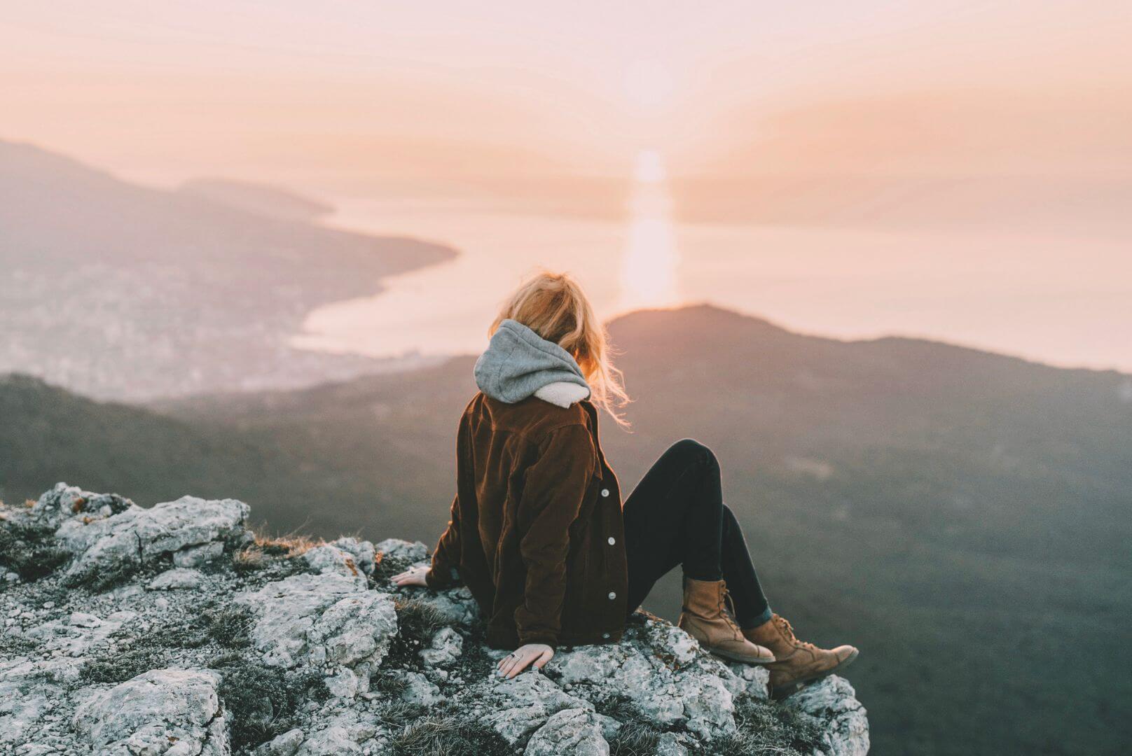 woman on cliff watching sunset and water