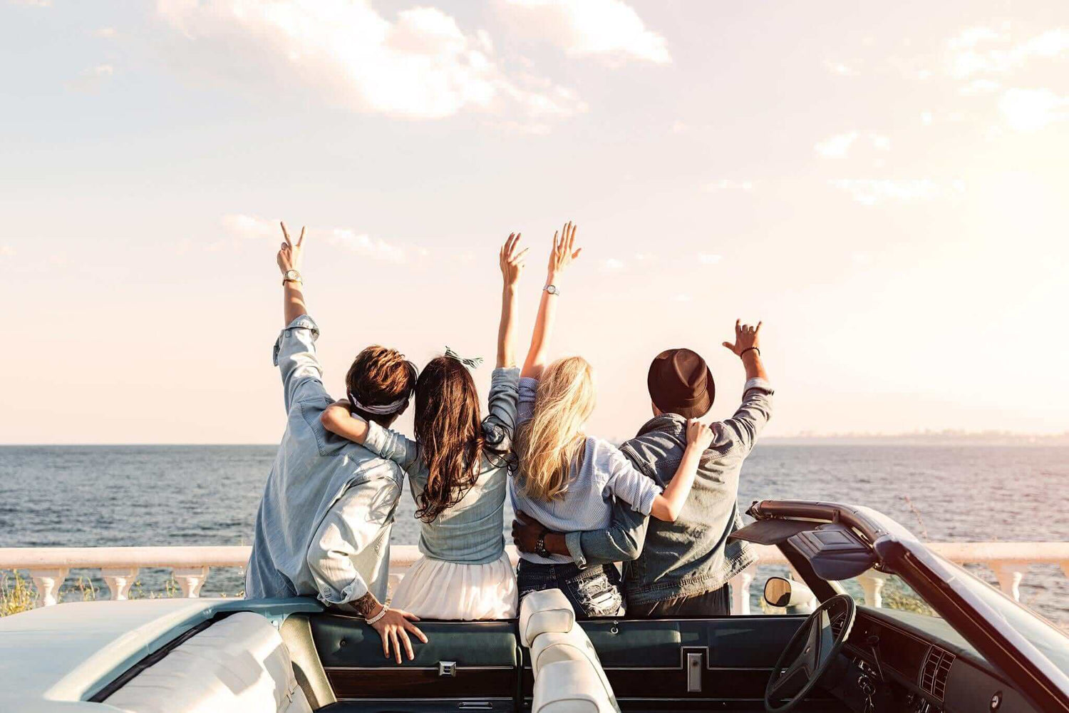 friends standing next to car looking over the water with hands raised in excitement