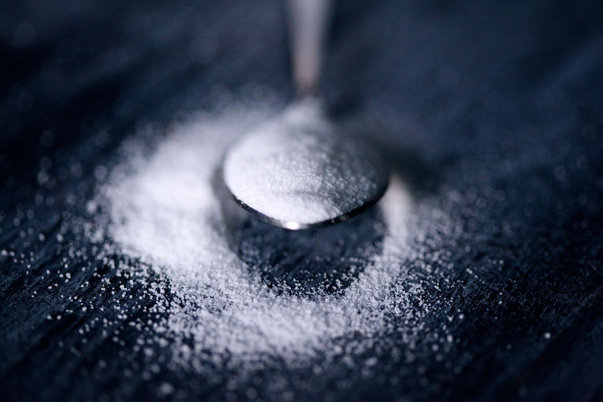 spoon with sugar on dark surface