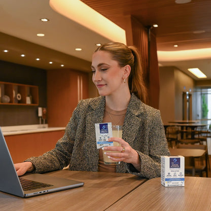woman in suit jacket in hotel sitting with laptop and smiling and holding well traveled packet and glass